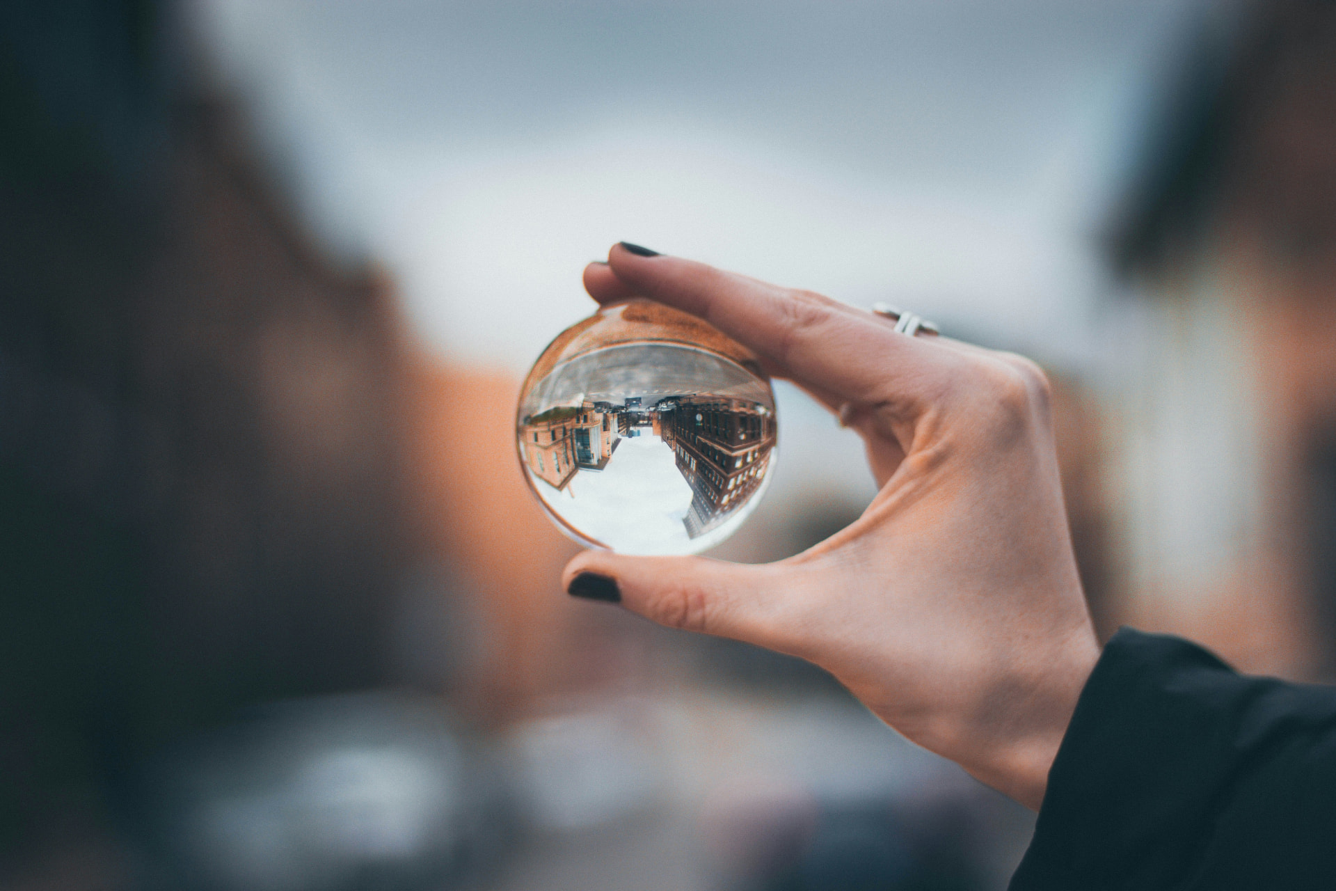 A hand holding a clear glass lens ball that reflects an inverted view of street buildings