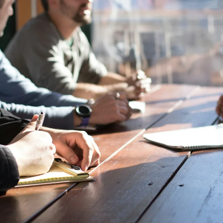 A team taking notes around a sunlit wooden table during a working session